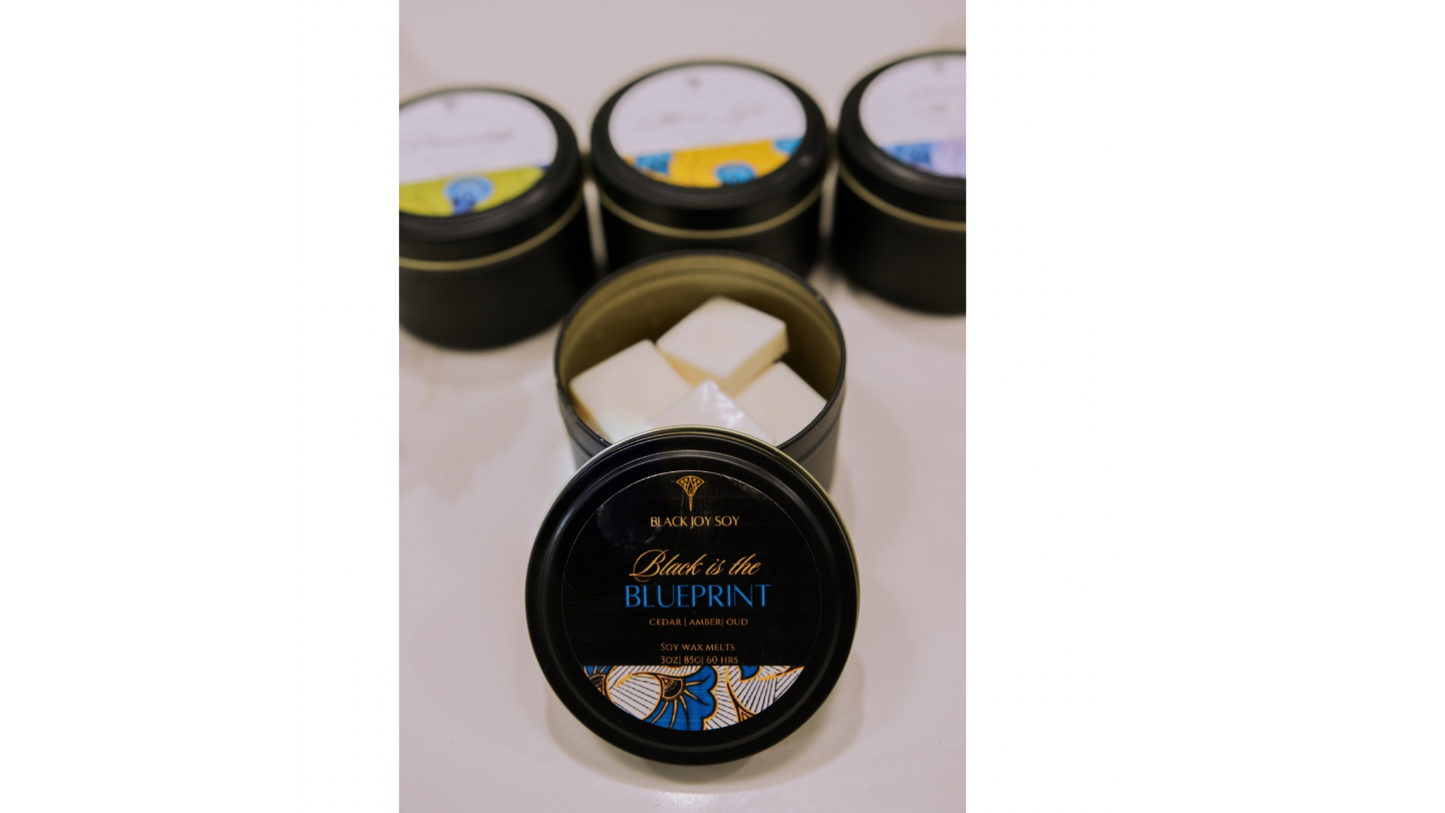 black metal tin with 16 amber, red cedar and oud scented wax melts inside. The tin has a black label with gold and royal blue accents/ writing. The words "Black is the Blueprint" are typed onto the label.