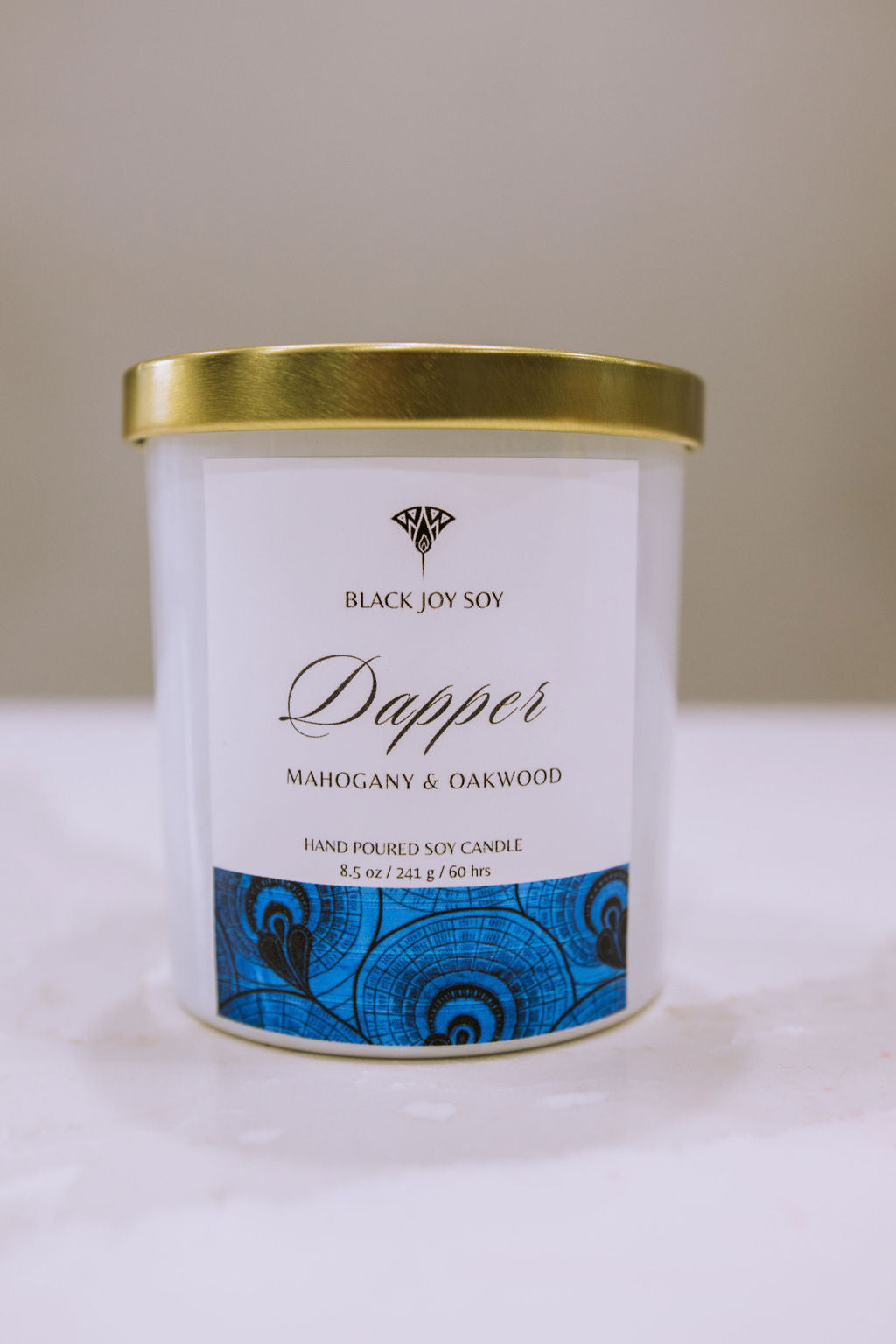 This is a 8.5 ounce Mahogany & Teakwood scented candle named "Dapper" in a white jar with a gold lid, and a bold royal blue label.