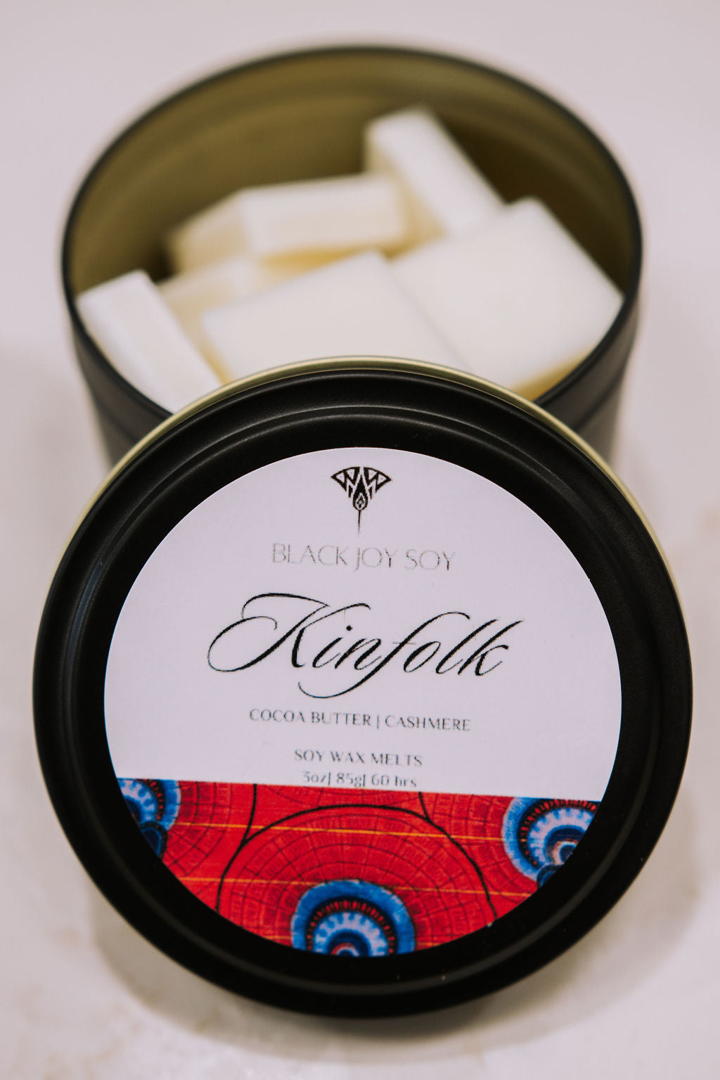 black metal tin with 16 Cocoa Butter & Cashmere scented soy wax melts inside. the tin lid has a red label on it with the word "Kinfolk" on it.