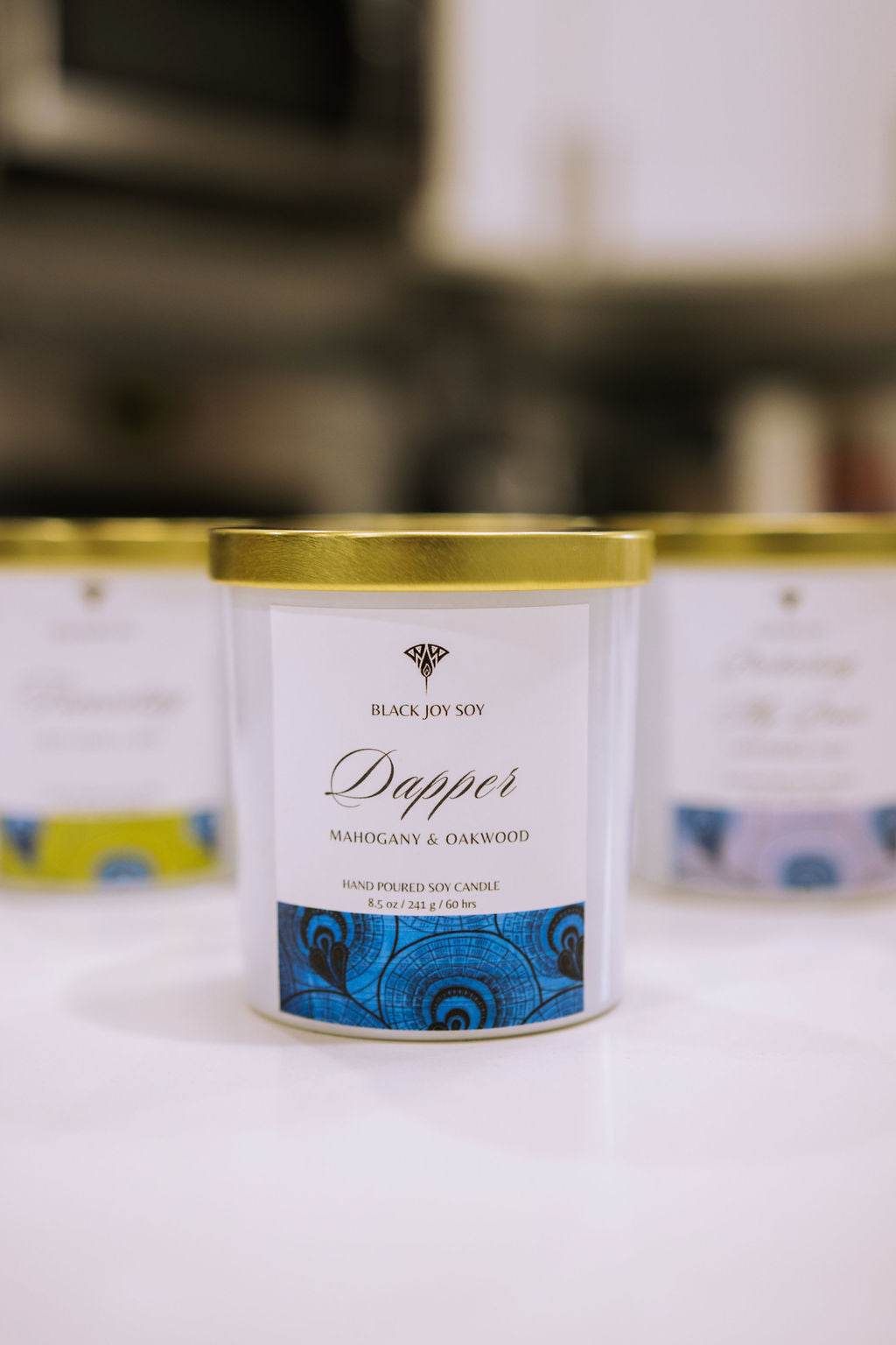 This is a 8.5 ounce Mahogany & Teakwood scented candle named "Dapper" in a white jar with a gold lid, and a bold royal blue label.