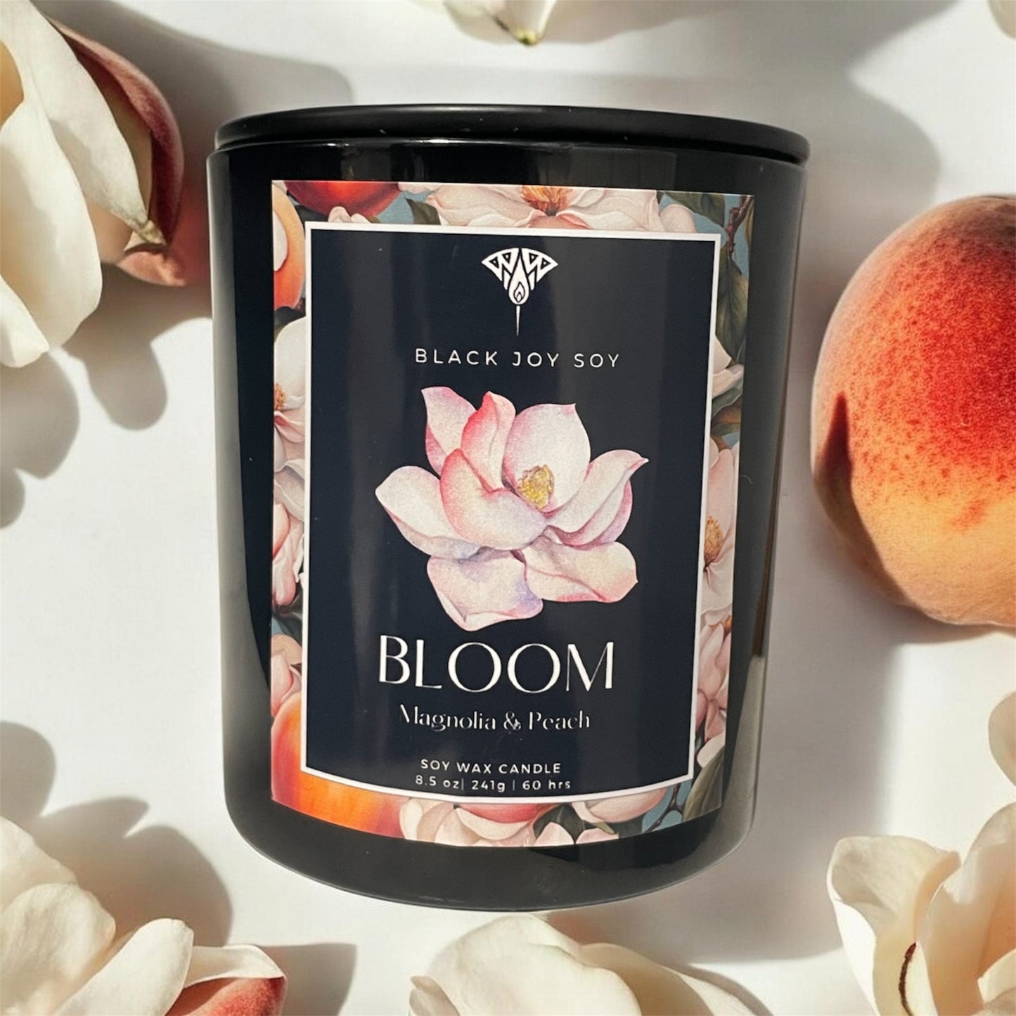 Candle with 'Black Joy Soy' branding and 'Bloom' fragrance label, surrounded by flowers and peaches. Peach scented candle. Floral scented candle. Spring candle. Soy candle. Gift. Hand poured artisan candles.