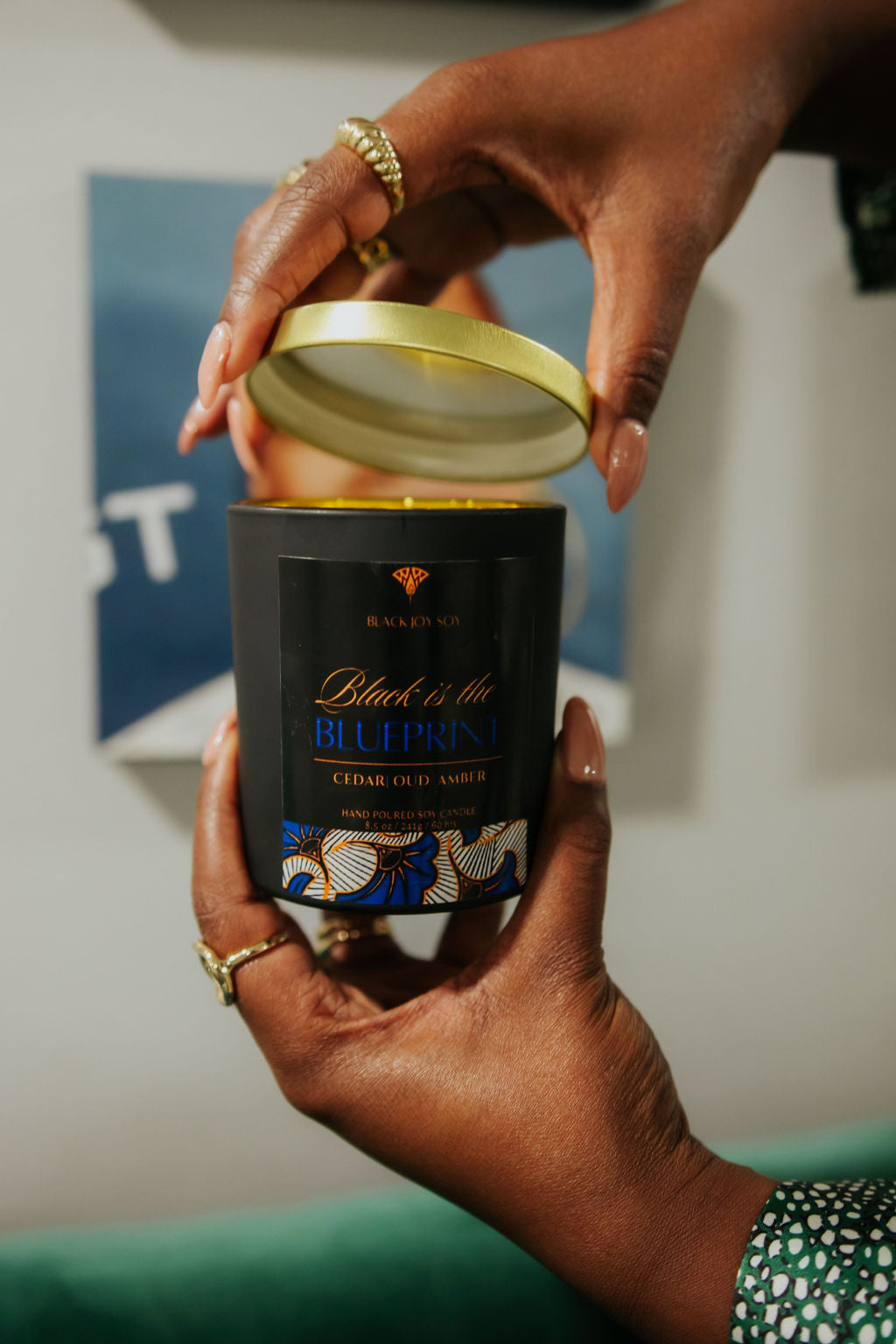 This is an 8.5 ounce amber, red cedar and oud scented candle named "Black is the Blueprint" in a black jar, with a gold lid, and a black, royal blue and gold label.