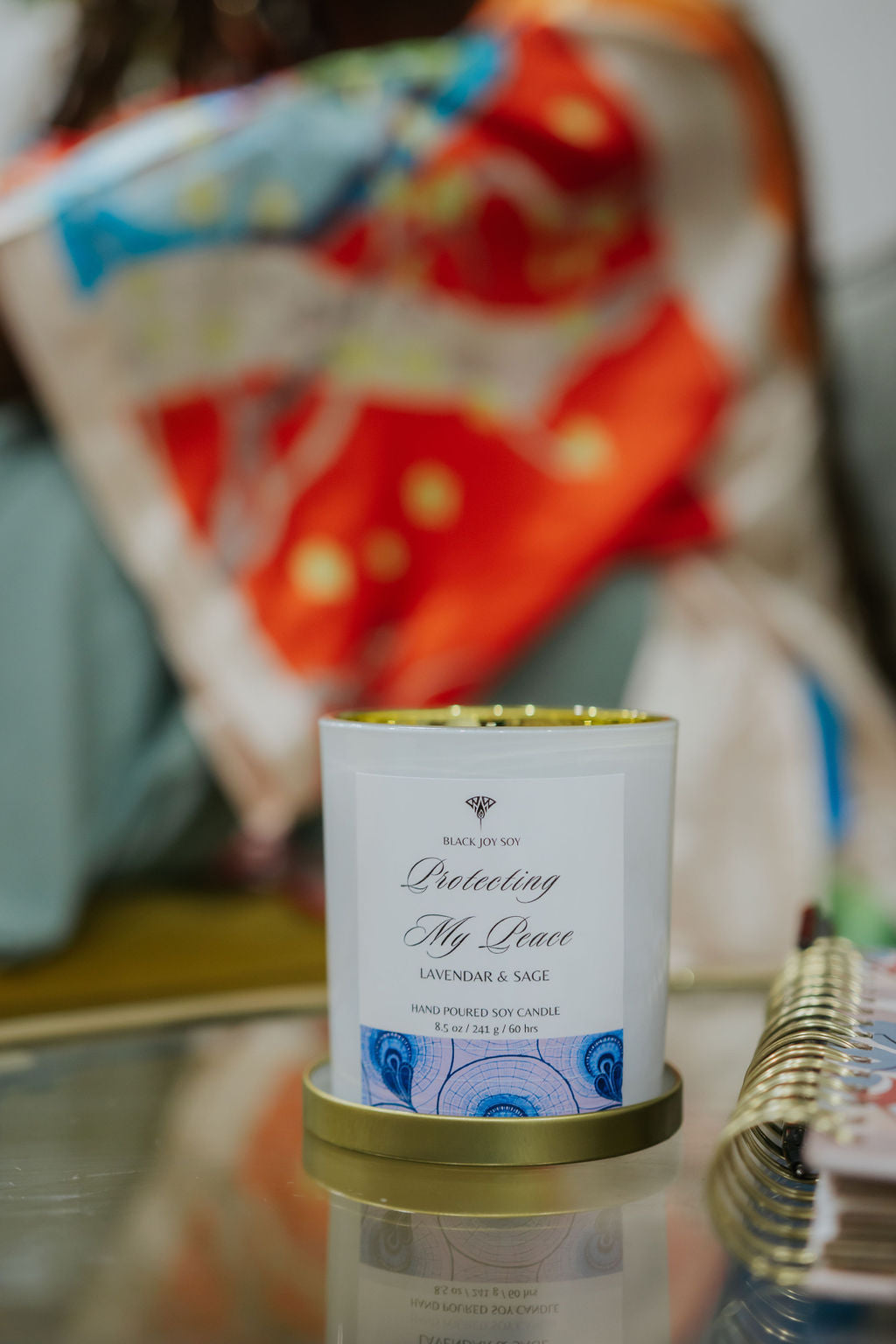 The foreground depicts an 8.5 ounce Lavender Sage & Vanilla scented candle in a white jar white a purple label.