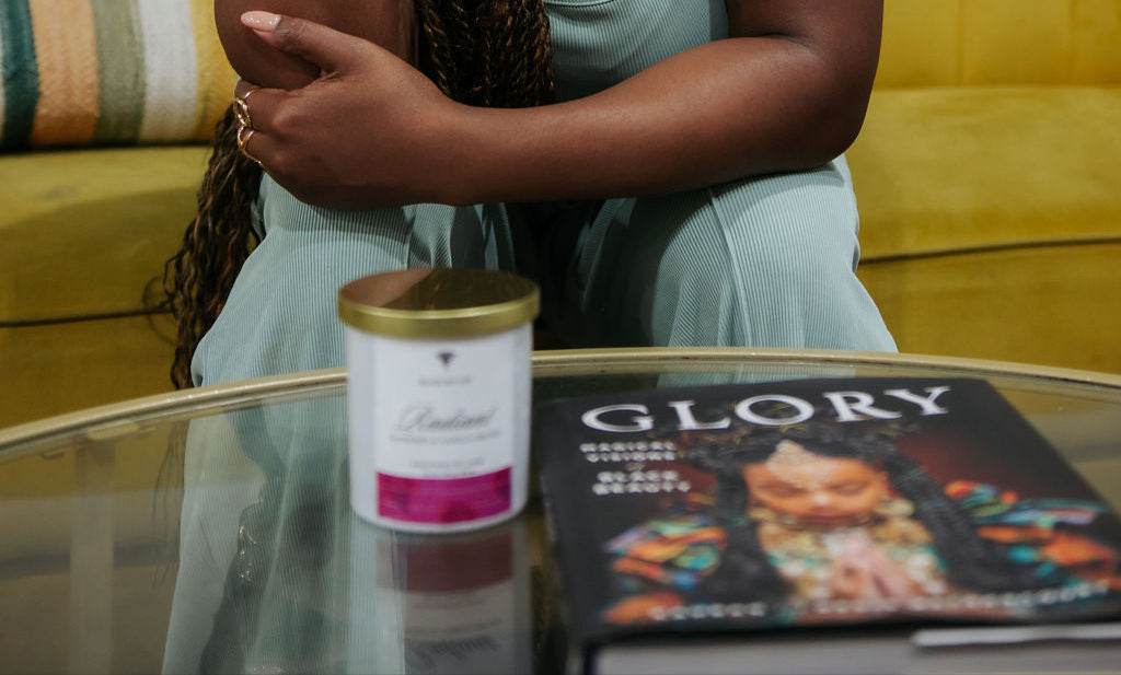 raspberry vanilla scented Soy candle with a pink label sitting on a table beside a book