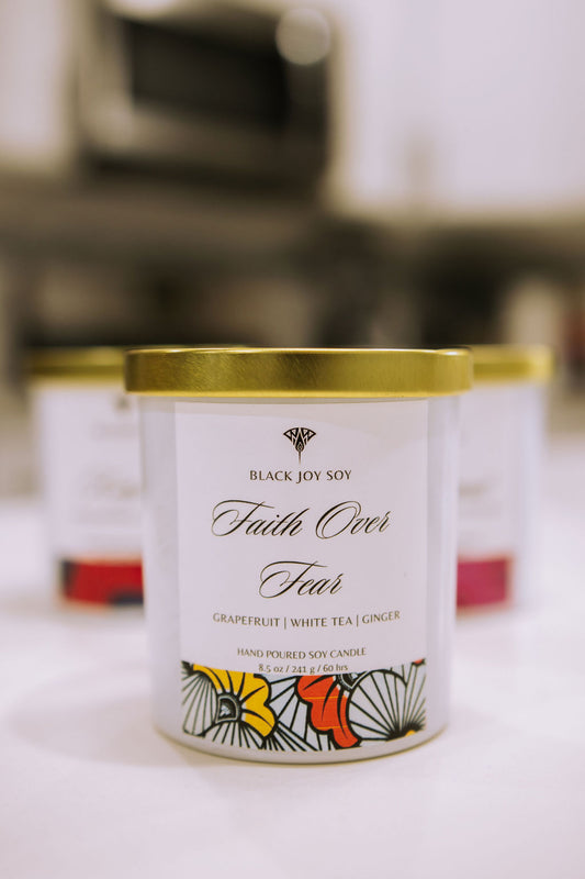 This is a 8.5 ounce Grapefruit, white tea & ginger scented soy candle named "Faith Over" in a white jar with a gold lid, and a red, yellow and white label.