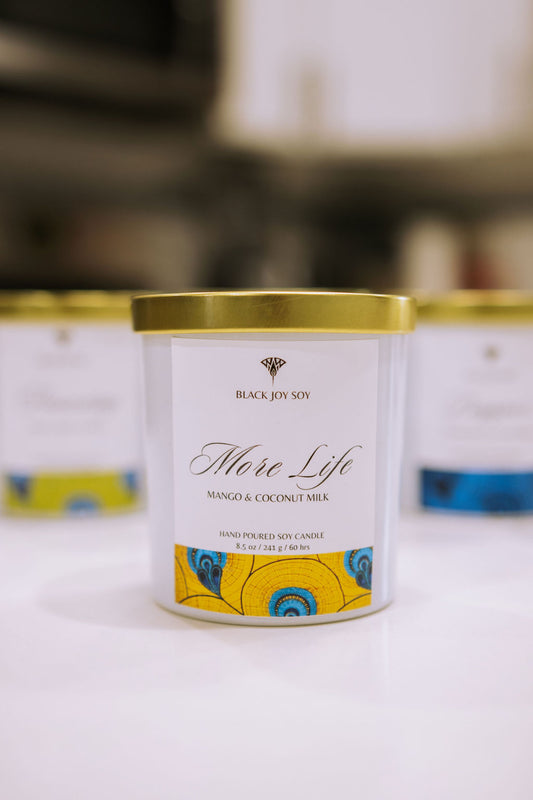 This is a mango and coconut scented soy candle named " More Life". It has a vibrant yellow and blue label.